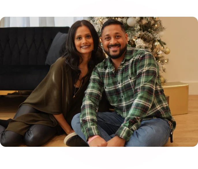 A man and woman sitting on the floor next to a christmas tree.